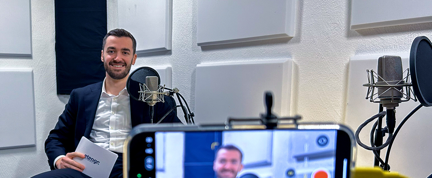 COO Christoph Kugelmannen sitzt in einem Tonstudio. Er hält einen Fragekatalog zu NIS-2 in der Hand. Im Vordergrund ist ein Smartphone zu sehen, das den Expertentalk-1 aufnimmt.